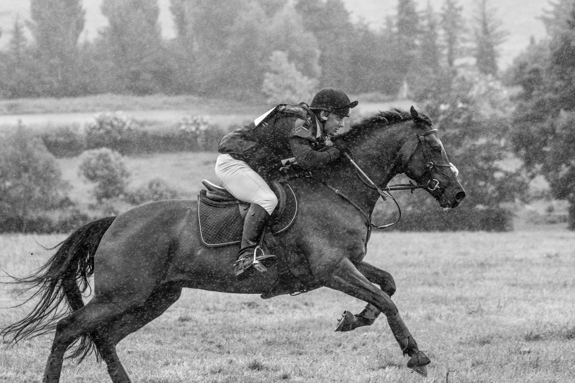 black and white photo pf a horse and rider galloping in the rain