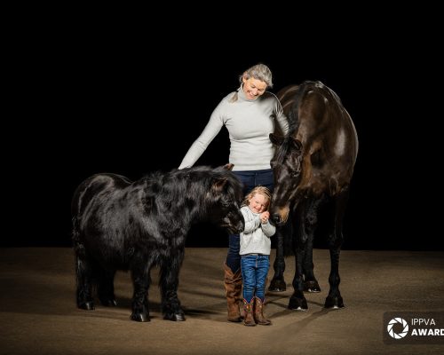 a mother and daughter in a family portrait with horses and a black background